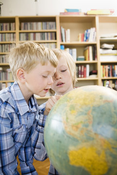 Boy showing brother map on globe at home