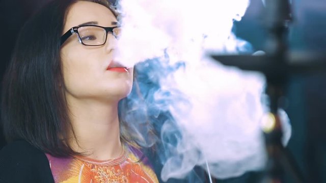 Beautiful girl smokes a hookah in a night bar