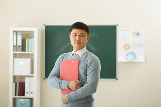 Handsome Asian Teacher With Clipboard In Classroom