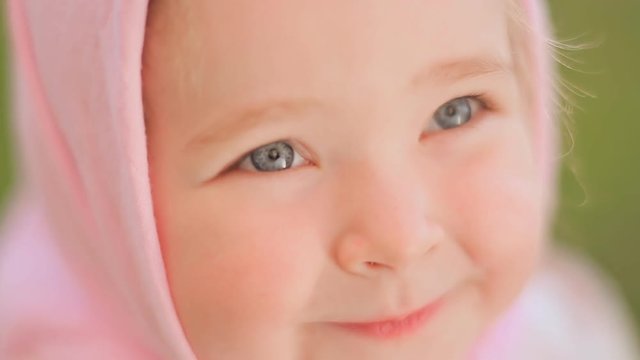 Little Russian girl posing in front of the camera. Smiling and looking close up. On the head is a pink headscarf.