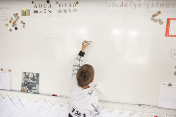 Rear view of boy writing on whiteboard in classroom