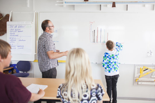 Boy drawing bar graph on whiteboard in classroom
