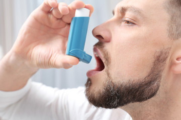 Young man using asthma inhaler, closeup - obrazy, fototapety, plakaty