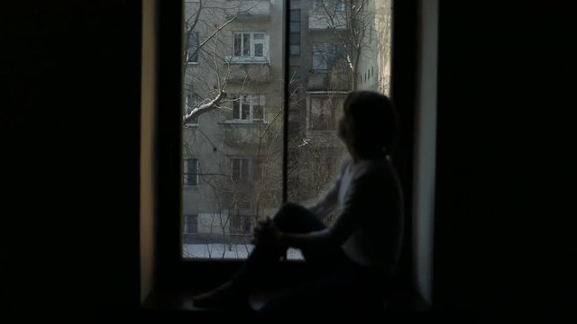 Silhouette of woman sitting on the windowsill and looking out the window