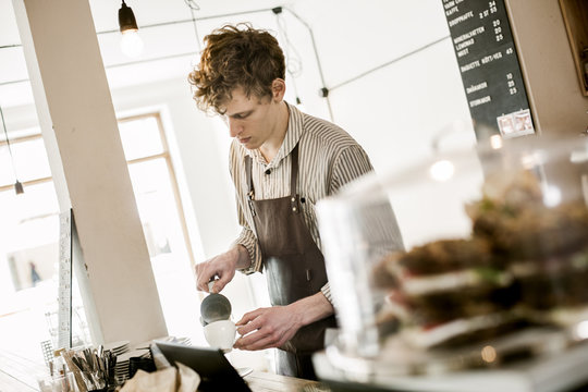 Young barista making cappuccino in coffee shop