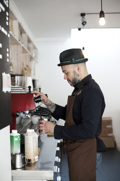 Side view of mid adult barista preparing coffee in cafeteria