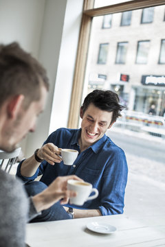 Smiling mid adult man enjoying coffee with friend at cafe