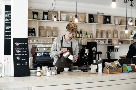 Young barista preparing cappuccino at counter in coffee shop