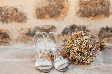 Wedding shoes of a bride on a stone background and a white bridal bouquet. Wedding in Montenegro.
