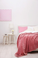 Comfortable bed with soft pink coverlet and pillows in light modern room