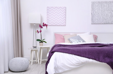 Comfortable bed with soft lilac coverlet and pillows in light modern room