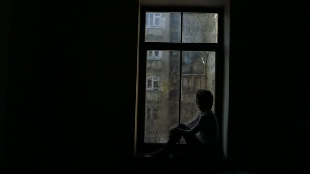 Silhouette of a woman sitting on the sill and looking out the window