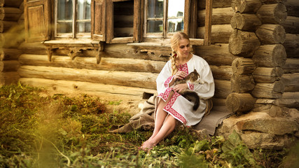 russian woman with a cat near old wooden house in a village