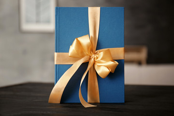 Book with ribbon as gift on wooden table