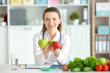 Young female nutritionist with apples in her office