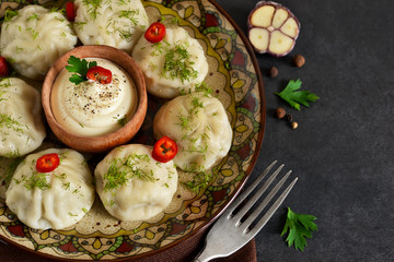 Khinkali with meat and spices with spicy cream sauce and garlic on a black background.