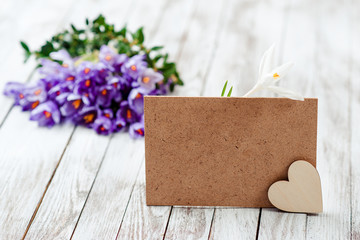 Beautiful crocus flowers in a basket near empty card for your text on wooden background.