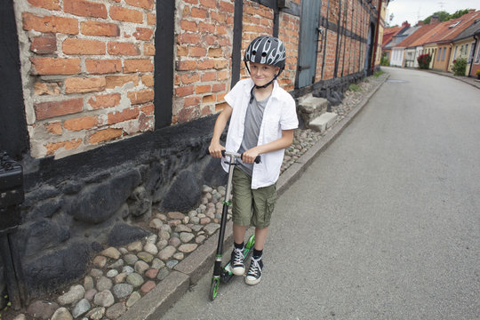 Portrait of happy boy riding push scooter on street in town