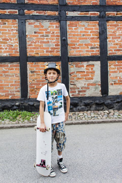 Portrait of confident boy standing with skateboard against brick wall