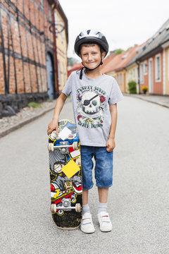 Portrait of happy boy standing with skateboard on street in town