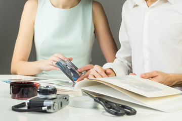 Looking and sorting love story wedding photographs. Young married or engaged couple puts analog printed pictures into wedding family photoalbum