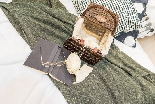 The modern fabric pillow with wicker basket, book, glasses and knitting sets on a white luxury bed