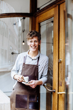 Portrait of smiling male barista holding coffee cup outside shop