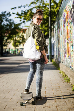 Full length portrait of confident woman standing on skateboard at sidewalk