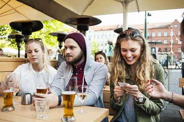 Happy woman reading visiting card while sitting with friends at sidewalk cafe