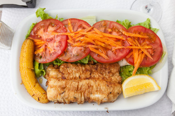 Traditional portuguese dish: scabbardfish (espada) with banana and tomato salad and lemon. Cuisine of Madeira island 