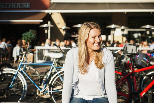 Happy woman sitting against sidewalk cafe