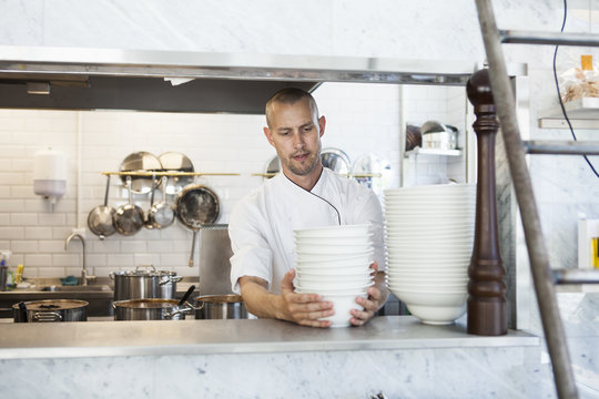Mid adult male chef stacking bowls at kitchen counter
