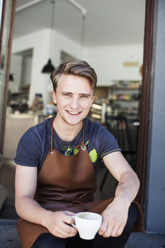Portrait of confident waiter holding coffee cup entrance
