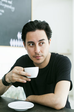 Thoughtful man holding coffee cup while sitting at table in cafe