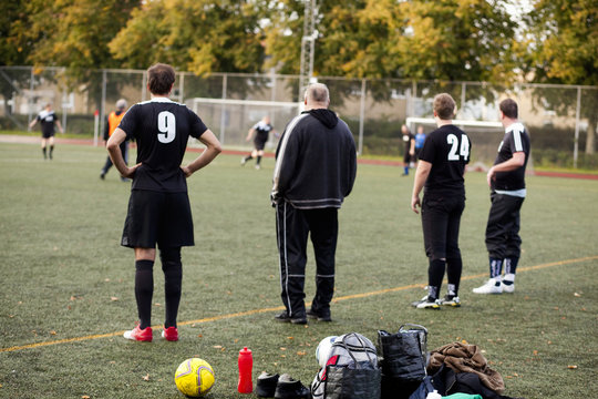 Rear view of soccer coach and players watching match on field