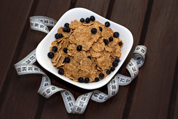 Corn flakes with berries in white plate on brown wooden boards. Nearby lies a meter. Background, texture, close-up. A side view of an angle