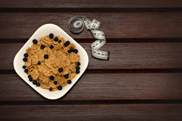 Corn flakes with berries in white plate on brown wooden boards. Nearby lies a meter. Background, texture, close-up. View from above