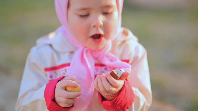 A little girl is eating a chocolate egg with a toy inside.