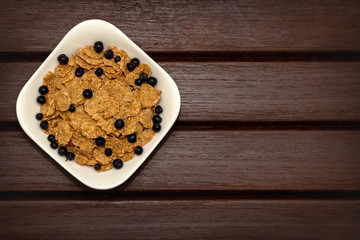 Corn flakes with berries in white plate on brown wooden boards. Background, texture, close-up. View from above