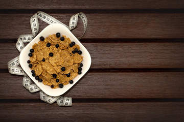  Corn flakes with berries in white plate on brown wooden boards. Nearby lies a meter. Background, texture, close-up. View from above