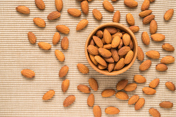 Almonds in brown bowl on place mat background, top view