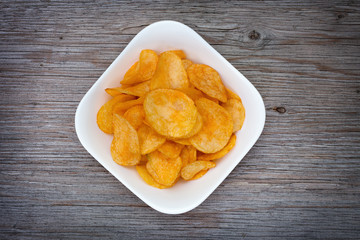 Salted potato chips in white bowl  on  gray wooden table. Close up. View from above