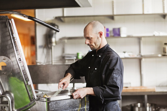 Chef frying potatoes in container at restaurant