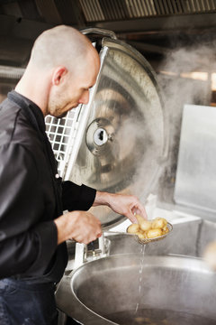 Side view of chef frying potatoes in container at restaurant