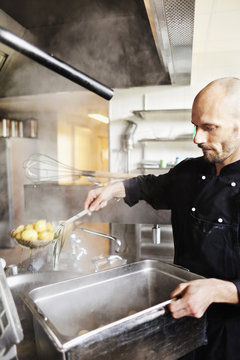 Male chef frying potatoes in container at restaurant