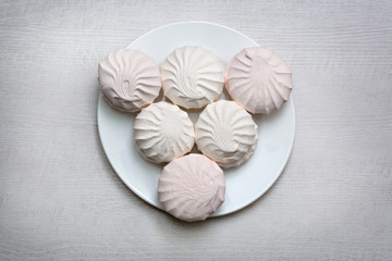 Marshmallow - zephyr in white plate on a light wooden table. Close up. View from above