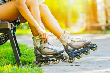 Young woman in park putting on roller blades on sunny summer day