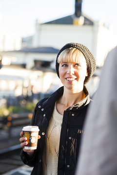 Happy woman with coffee cup on sunny day at railroad station