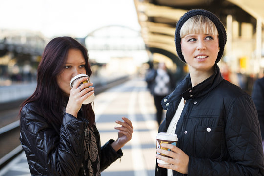 Young female friends with coffee on railroad station