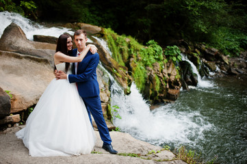 Lovely wedding couple against waterfall on sunset at Carpathian mountains.